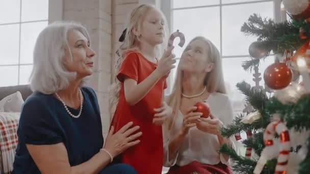 Vrouw, grootmoeder en een meisje versieren een kerstboom, praten en glimlachen — Stockvideo