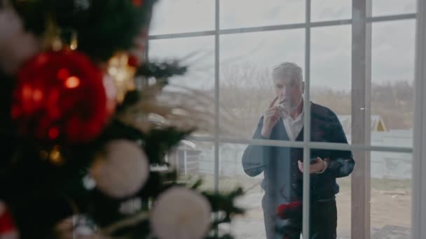 Avô está fumando lá fora, olhando pela janela na árvore de Natal — Vídeo de Stock