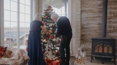 Büyükannem ve büyükbabam Noel ağacını süslüyor, konuşuyor, gülümsüyor ve sarılıyorlar.