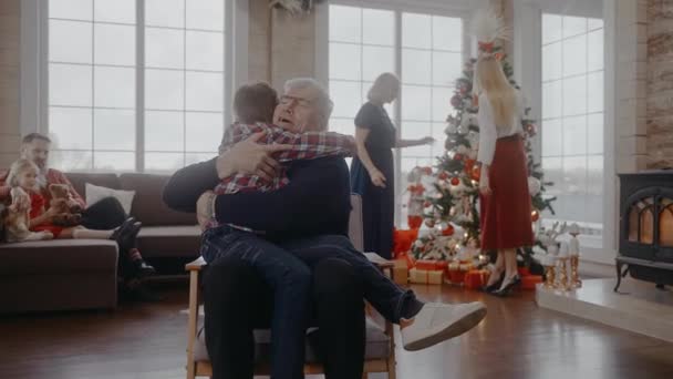 Nagyapa megöleli az unokáját, amint egy széken ül Szenteste. — Stock videók