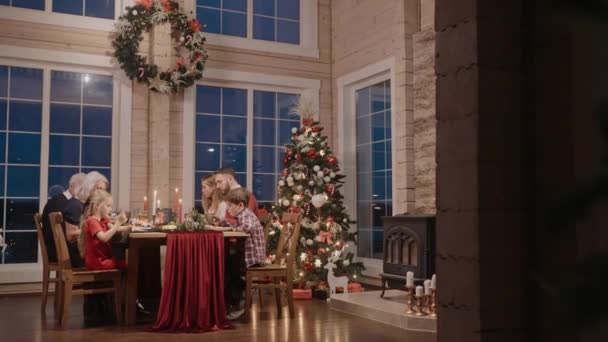 Toda la familia hablando y comiendo en la mesa en Nochebuena, filmada desde lejos — Vídeos de Stock
