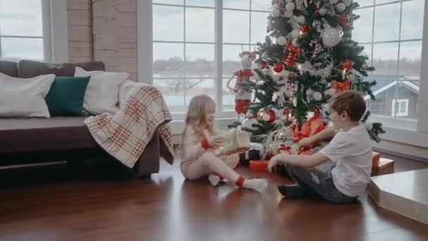 Мальчик и девочка бегут открывать подарки под елкой рождественским утром — стоковое видео