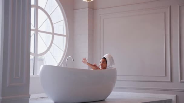 Чорна жінка лежить у ванні, миючи руки з волоссям, загорнутим у рушник — стокове відео