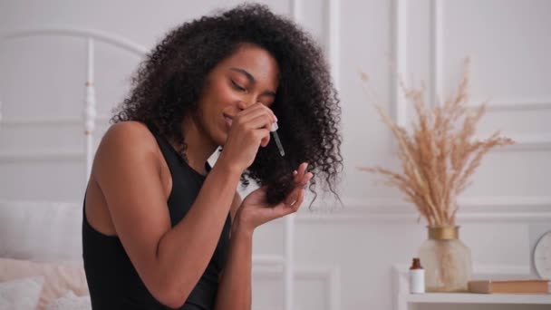 Black woman applies cosmetic oil from a bottle with dropper on her afro hair — Stock Video