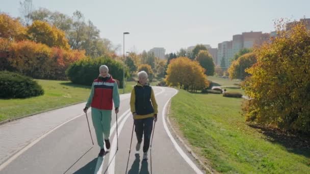 Zwei betagte Frauen beim Nordic Walking im Herbst Stadtpark an einem sonnigen Tag, Frontansicht — Stockvideo