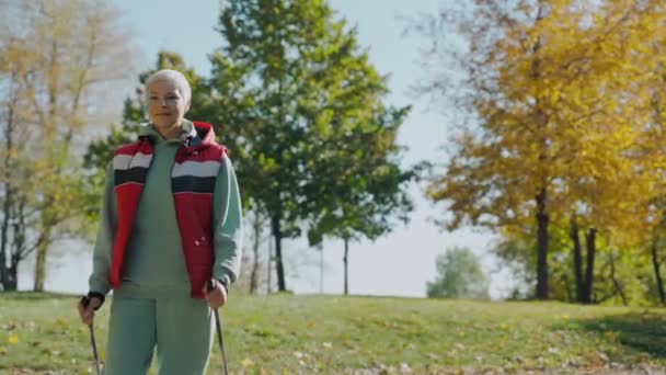Ältere Frau beim Nordic Walking im sonnigen Herbstpark allein, Frontansicht — Stockvideo
