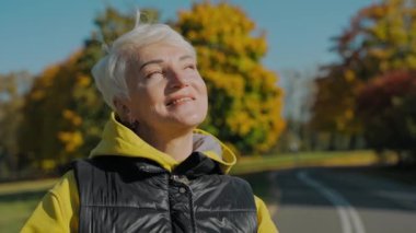 Genç ve sportif bir kadının sonbahar parkında güneşe bakıp kameraya bakması.