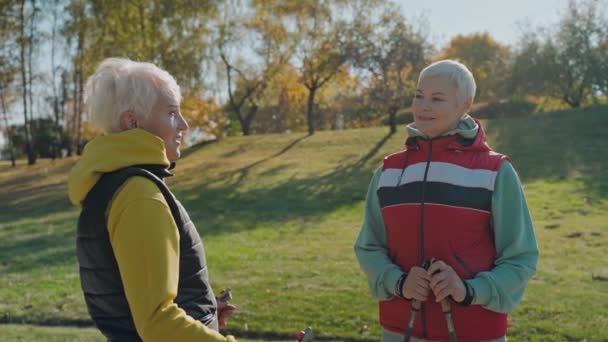 Dvě staré ženy mluví ve slunečném podzimním parku, nosí vesty a drží vycházkové hole — Stock video