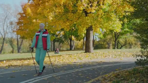 Ältere Frau beim Nordic Walking im sonnigen Herbstpark allein, Frontansicht — Stockvideo