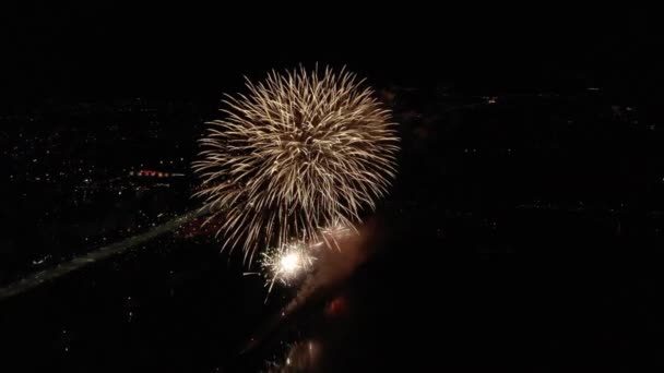 Vários fogos de artifício explodem sobre o rio perto da cidade à noite, disparados com drone — Vídeo de Stock