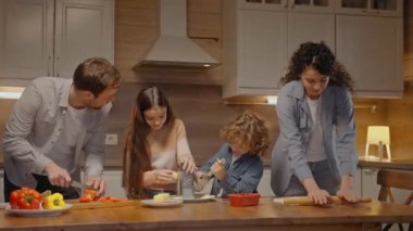 Aile evde birlikte yemek pişiriyor, gülüyor ve çocuklarla konuşuyor.