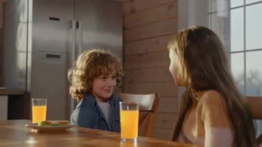 Küçük çocuk ve kız kahvaltıda gülümsüyor ve konuşuyor, portakal suyu içiyor.