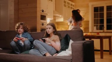 Çocuklar oyun konsolunda aktif olarak oynuyor, aileler arka planda dans ediyor.