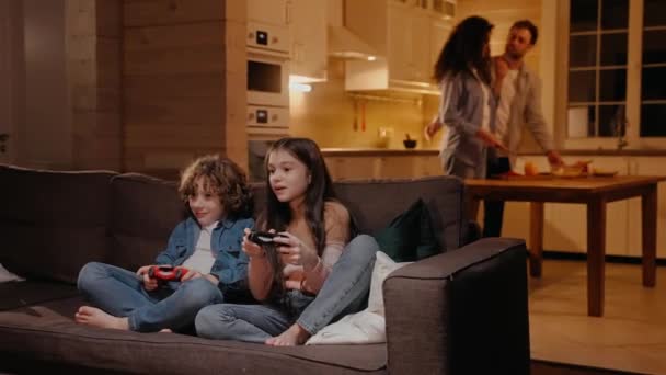 Dzieci bawią się na konsoli do gier, rodzice przygotowują obiad w tle — Wideo stockowe