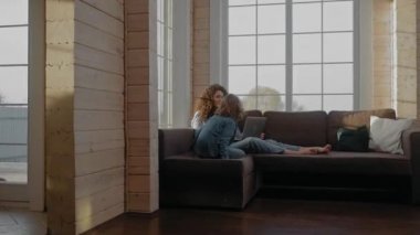 Çocuk laptopun başında çalışırken annesine koşuyor ve ona kanepede sarılıyor.