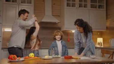 Aile evde yemek pişiriyor, çocuklarla gülüyor ve dans ediyor.