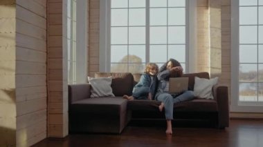 Çocuk laptopun başında çalışırken annesine koşuyor ve ona kanepede sarılıyor.