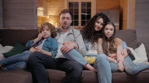 Familia viendo una película juntos en casa abrazándose y riendo con comedia — Vídeo de stock