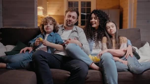 Família assistindo um filme juntos em casa abraçando, comendo batatas fritas e rindo — Vídeo de Stock