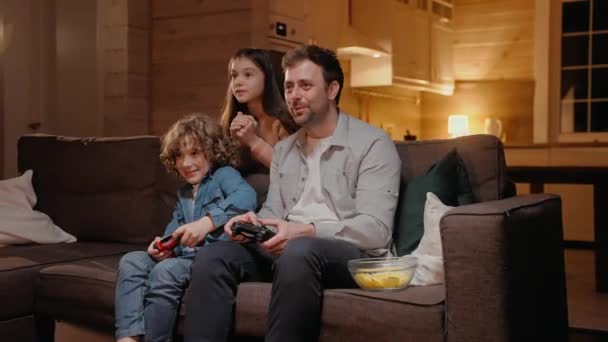 Padre jugando con su hijo en la consola de juegos y perdiendo, riendo sentado en el sofá — Vídeo de stock