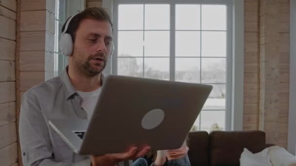 Homme avec écouteurs travaillant sur appel vidéo tandis que ses enfants s'amusent — Video