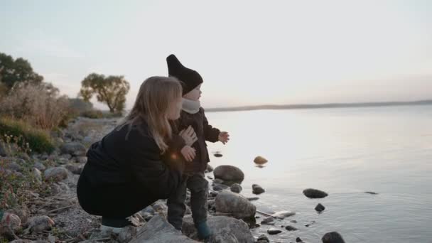Frau spricht an einem Herbstabend am Steinufer eines Sees mit ihrem Kind — Stockvideo