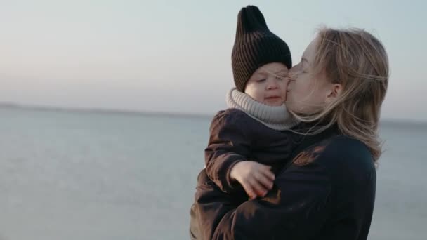 Een gelukkige vrouw houdt en kust haar baby naast een meer op een herfstavond — Stockvideo