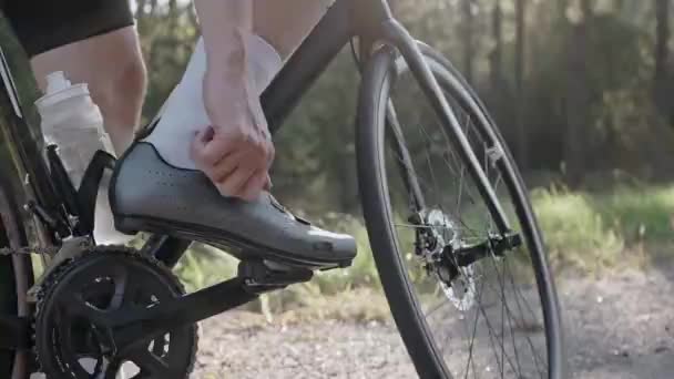 Man draait het contact fiets schoenen op een racefiets bij zonsondergang in het bos — Stockvideo