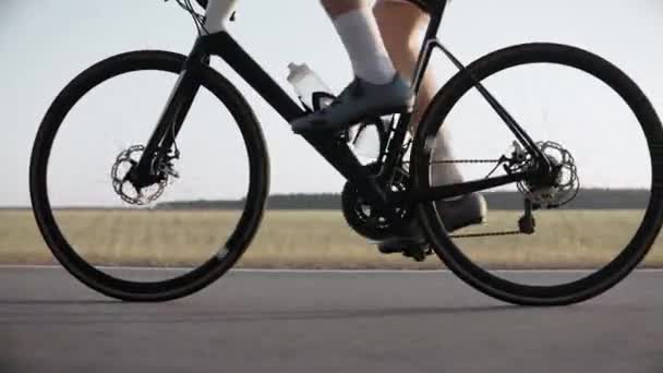 Close-up van de benen van een man op een racefiets op een snelweg bij zonsondergang — Stockvideo