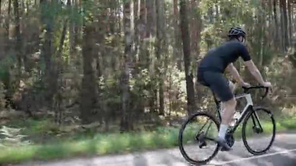 Muž cyklista vlaky tím, že jezdí na silničním kole ve slunném lese, nosí helmu — Stock video