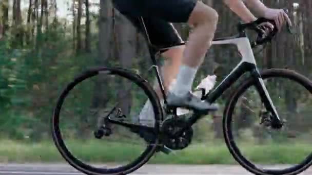 Close-up van de benen van een man op een racefiets in een zonnig bos — Stockvideo