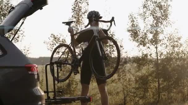 Homem remove uma bicicleta de estrada de uma bicicleta de carro montagem ao pôr do sol em uma estrada — Vídeo de Stock