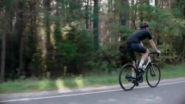 Egy férfi kerékpáros vonatok lovaglás egy közúti kerékpár egy napsütötte erdőben, visel sisakot — Stock videók