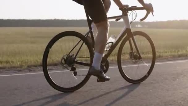Primo piano dell'uomo che guida una bici da strada al tramonto su un'autostrada, indossando il casco — Video Stock