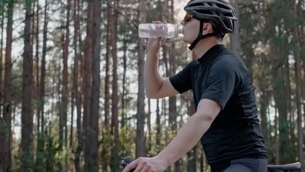 Samiec rowerzysta pije wodę po jeździe na rowerze w sosnowym lesie w słoneczny dzień — Wideo stockowe