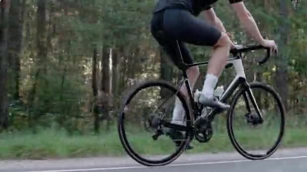 Tiro das pernas de um homem andando de bicicleta de estrada em uma floresta ensolarada — Vídeo de Stock
