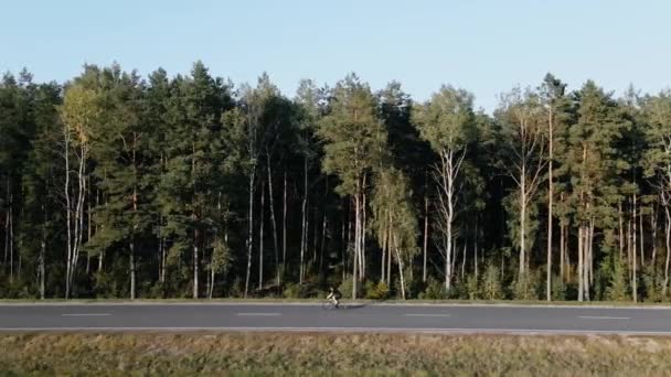 夏に森の近くの高速道路でロードバイクに乗るサイクリストのドローンショット — ストック動画
