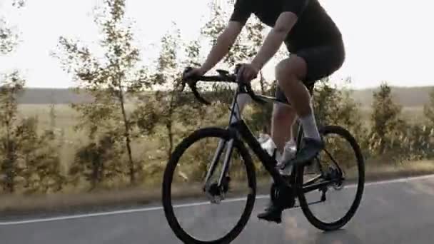 Чоловік їде на дорожньому велосипеді на заході сонця на шосе поблизу поля, в шоломі — стокове відео