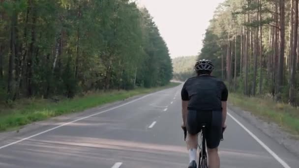 Tylne ujęcie człowieka jadącego na rowerze w lesie o zachodzie słońca, w kasku. — Wideo stockowe
