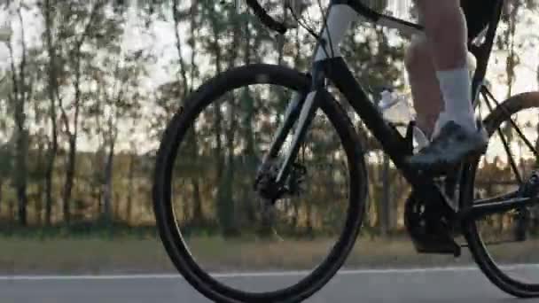 Close-up de um homem andando de bicicleta de estrada em uma estrada ao pôr do sol — Vídeo de Stock