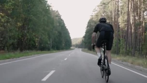 Shot from behind of a man speeding on a road bike in the woods, wearing a helmet — Stock Video