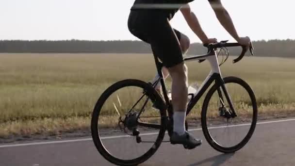 Lado tiro de homem andando de bicicleta de estrada ao pôr do sol em uma estrada, usando capacete — Vídeo de Stock