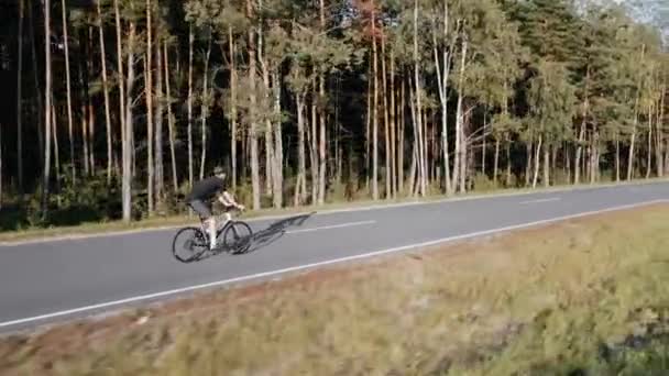 Aerial video of cyclist riding a road bike on a highway near forest in summer — Stock Video