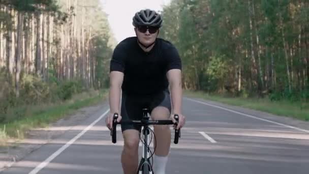Vue de face d'un cycliste en vélo de route dans une forêt ensoleillée, portant un casque — Video