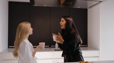 Genç esmer ve genç bir sarışın mutfakta pijamalarıyla dans ediyorlar.