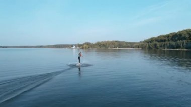 Hidrofolyo sörf tahtasına binen ve güneşli bir günde büyük mavi göle düşen bir adam.