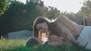 Anne, güneşli bir günde kızıyla çimlerin üzerinde oynayıp gülümsüyor.