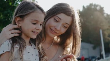 Küçük kız annesinin kucağında oturur, elinden uçan uğur böceğini seyreder.