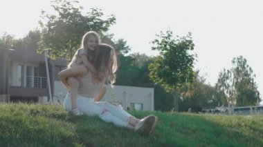 Küçük kız güneşli bir günde çimlerin üzerinde annesinin sırtına oturur.