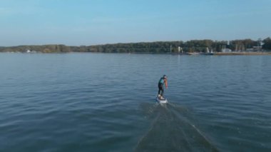 Güneşli bir havada, büyük mavi gölde, su folyosunun üzerinde sörf yapan bir adam.